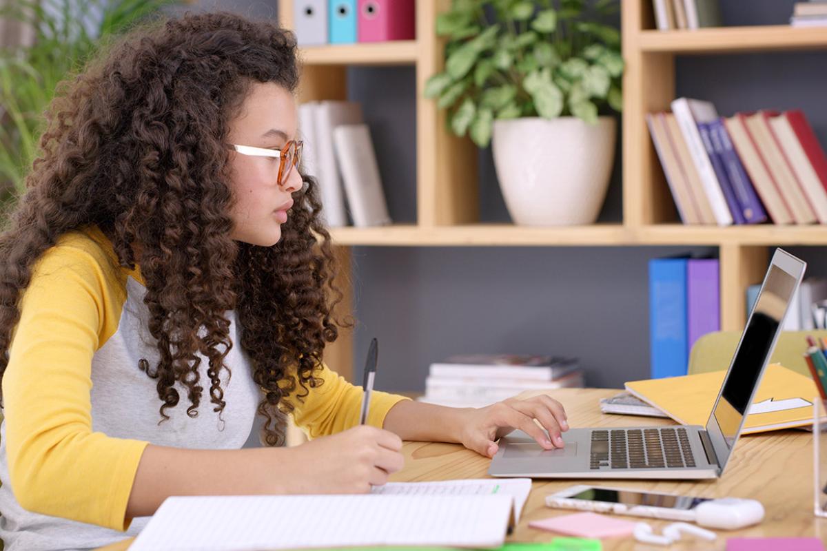 A young woman writing down notes on a pad while working on a laptop