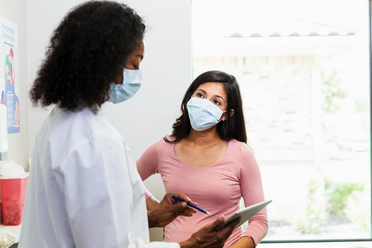A female physician and patient, both masked, reviewing the patient's chart