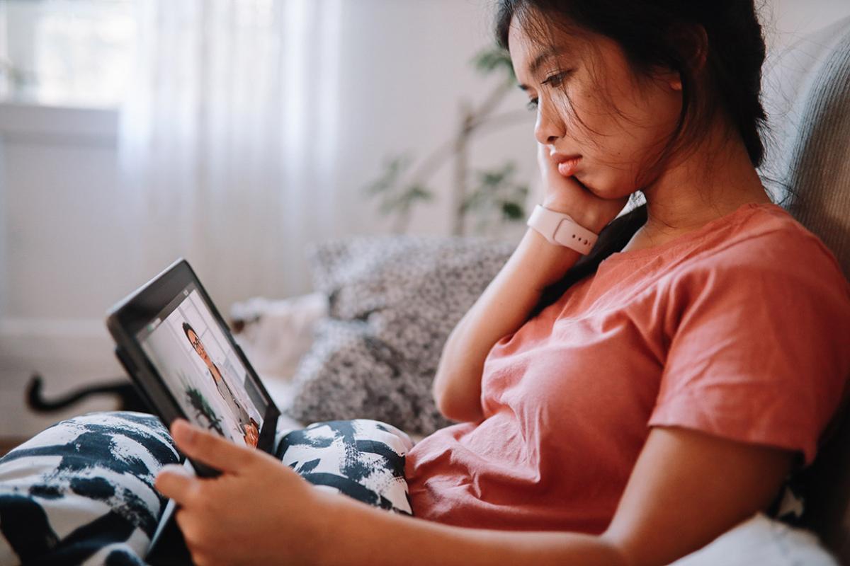 Woman sitting on a sofa with a computer tablet having a telehealth conference with a physician