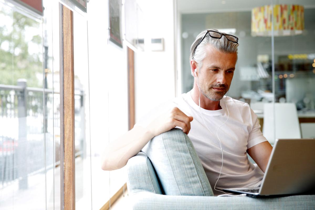 Man sitting on couch wearing ear buds and working on a laptop