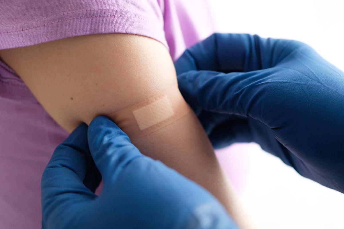 Very tight shot of gloved health professional applying an adhesive bandage after giving a child a vaccination on the right arm