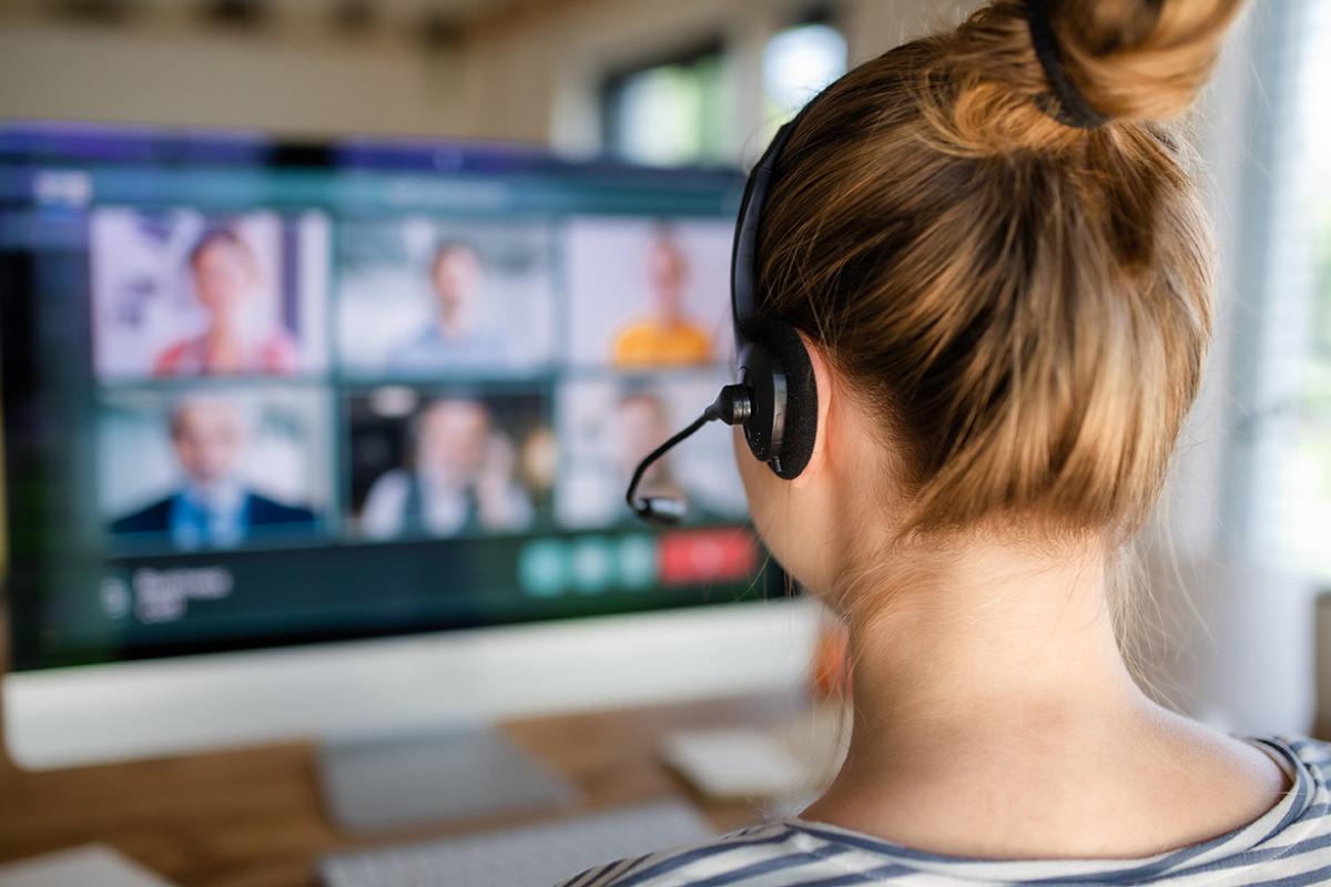 Shot from the back of woman wearing headphones and sitting at a desk taking part in a virtual meeting or conference