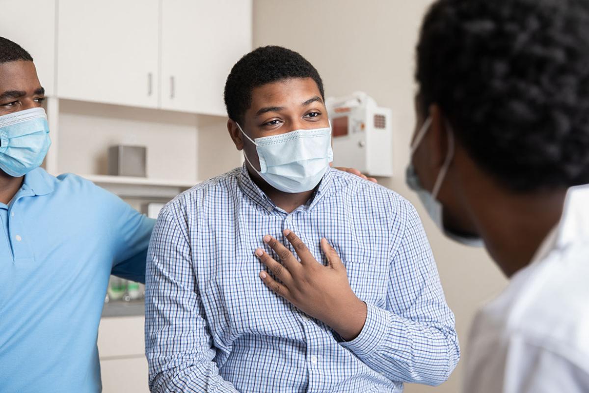 Masked patient holding hand to chest and speaking with physician