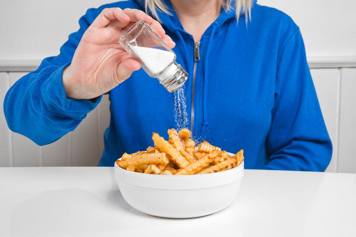 Person salting a bowl of french fries
