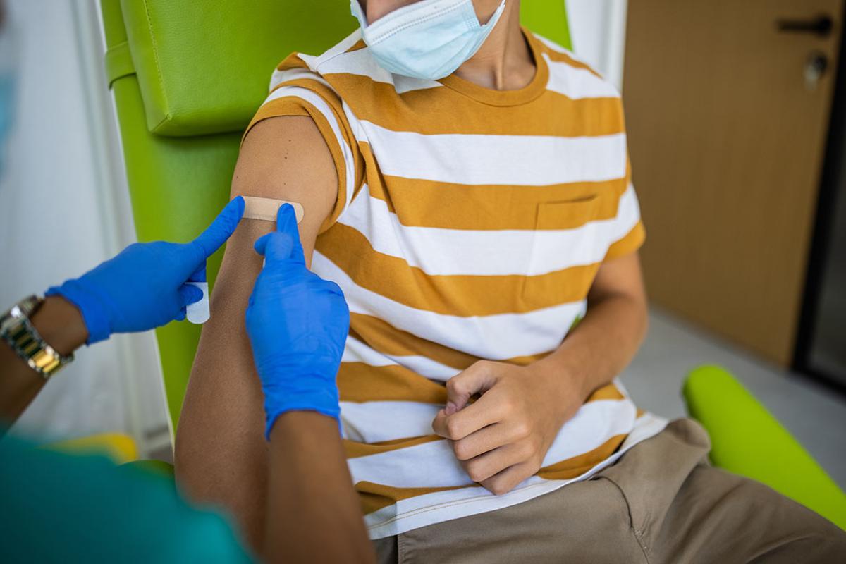 Health care worker putting bandage on young person's arm after vaccination