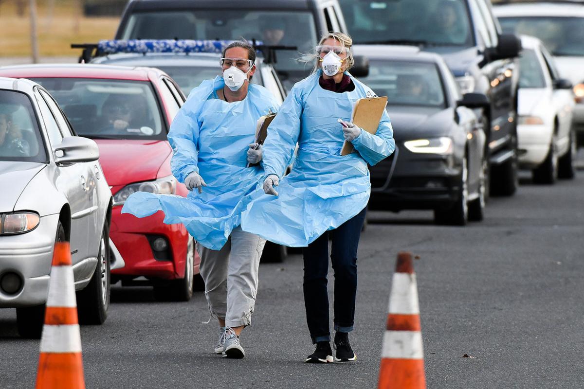 Two Colorado health care workers in gowns and PPE in parking lot set up for drive thru COVID-19 testing.