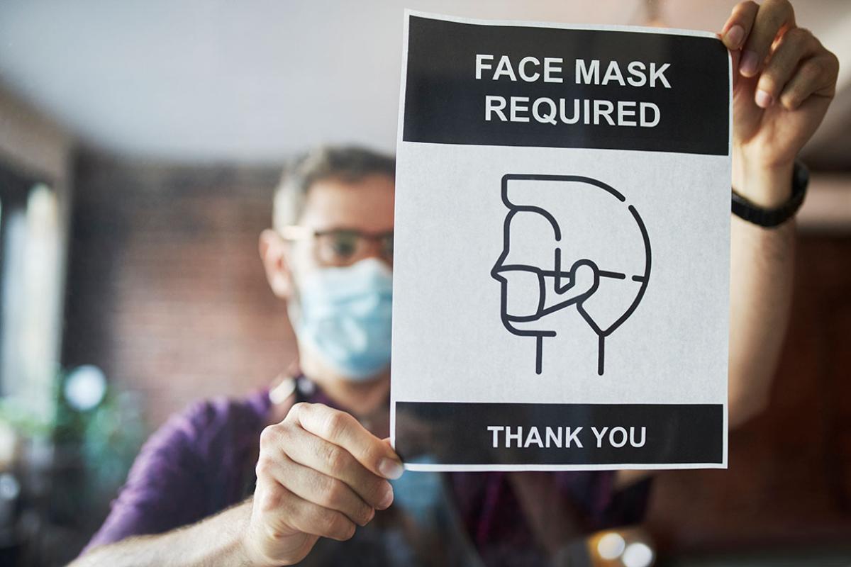 Business owner setting up face mask required sign in cafe window