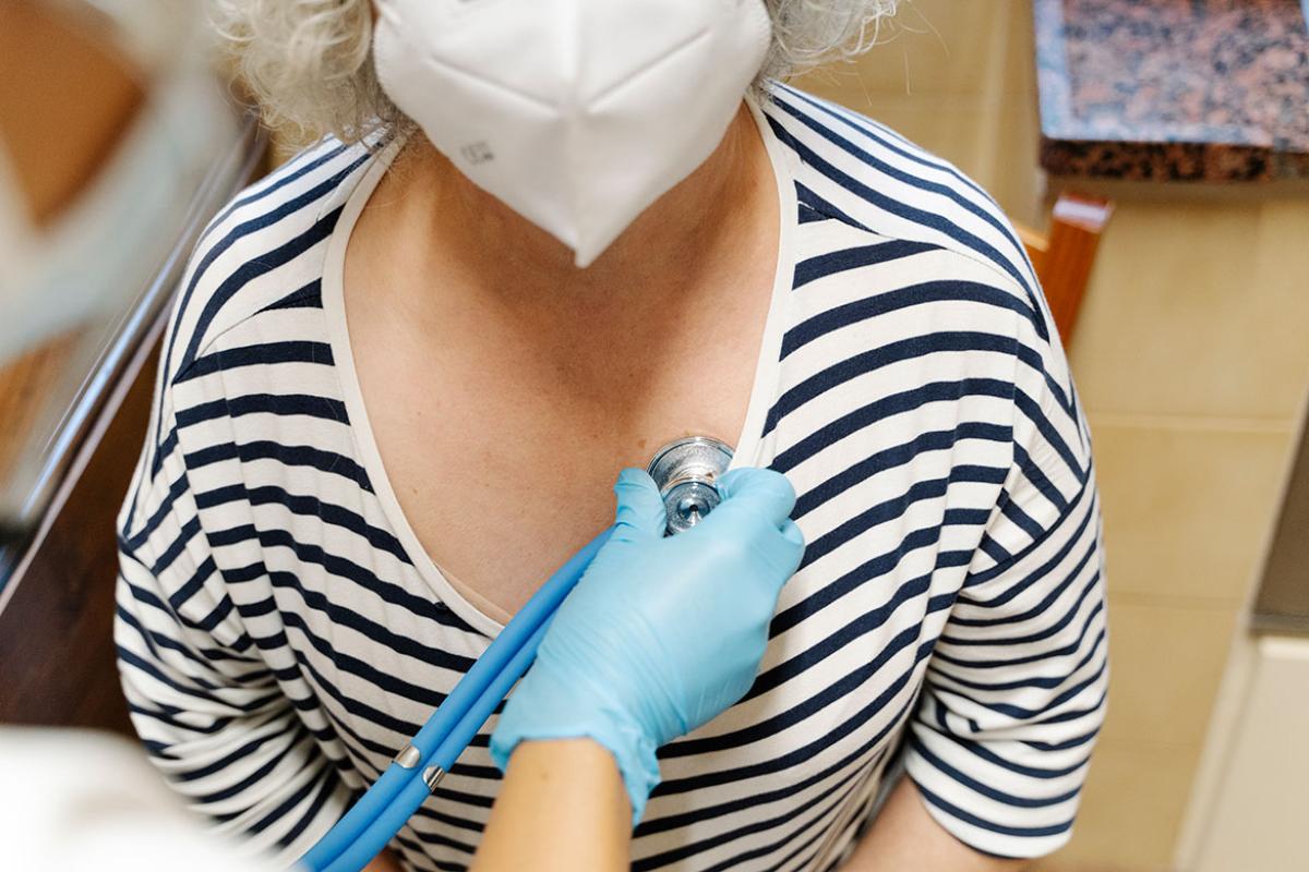 Physician examining the heart of an elderly person wearing medical mask with a stethoscope