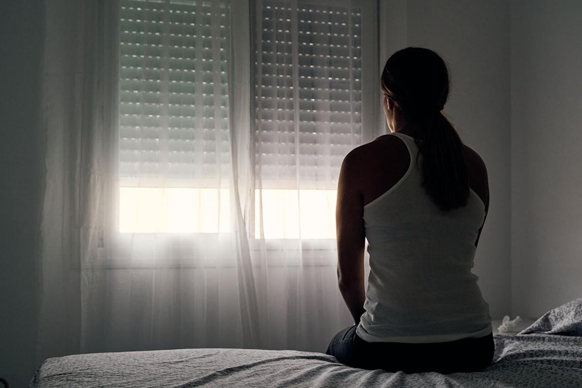 Rear view of woman sitting on a bed looking out the window