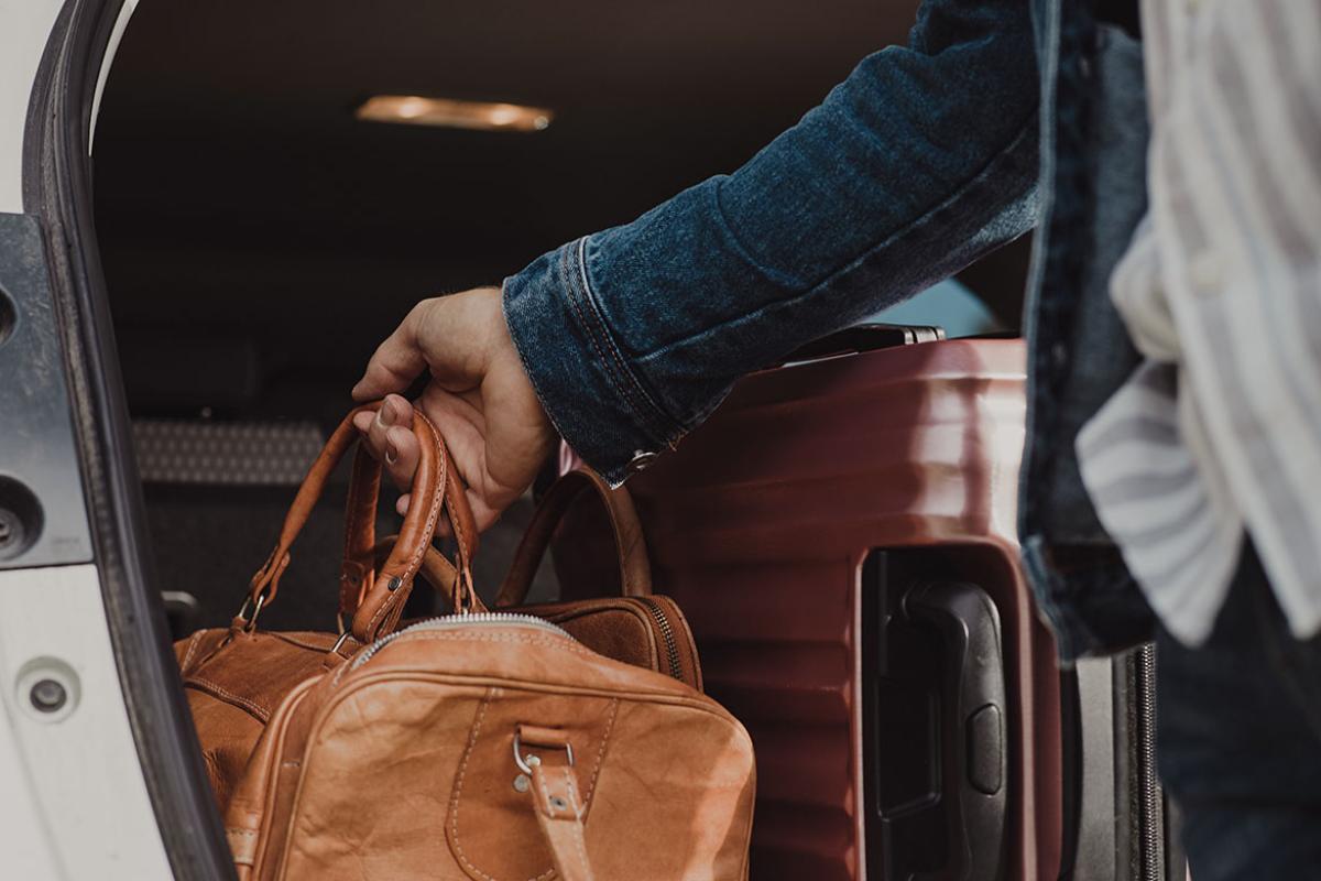Hand placing a suitcase in a car trunk