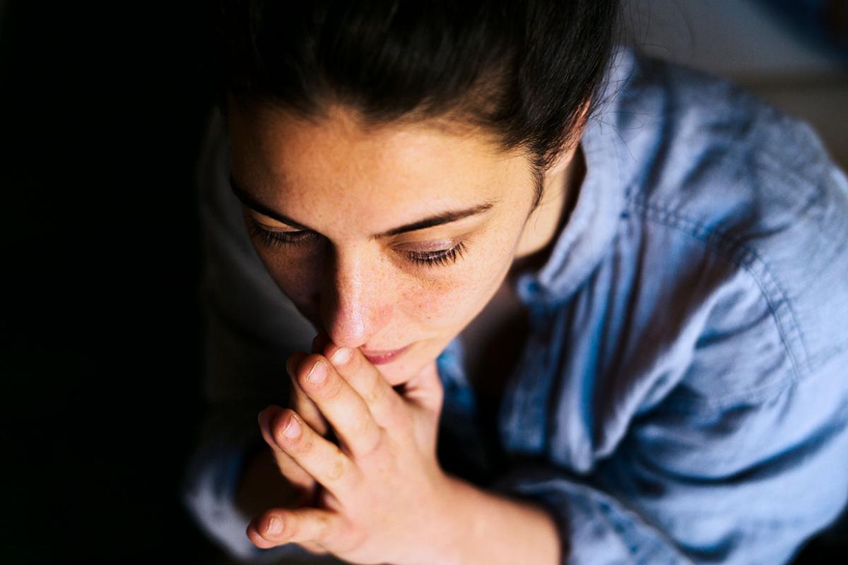 Woman in thought with hands clasped at chin