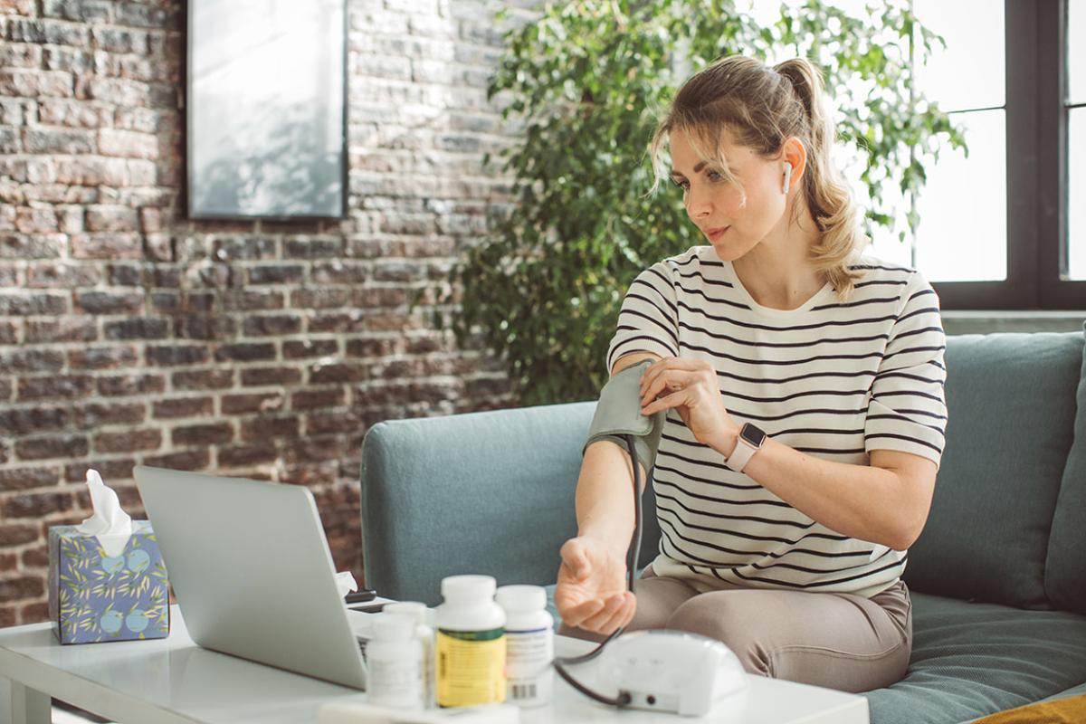 Person measuring blood pressure and consulting with someone via laptop