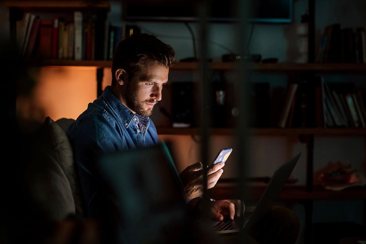 Person working at a laptop while looking at smartphone
