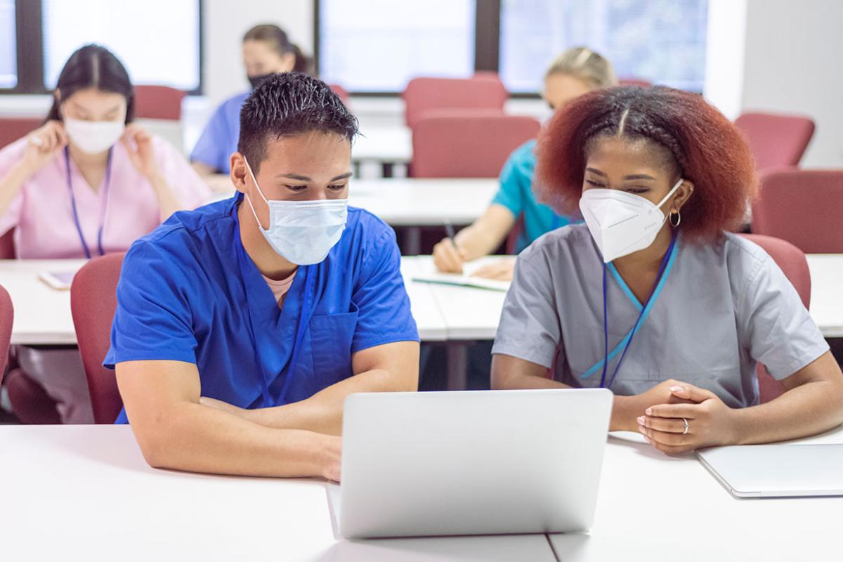 Two masked people working in front of a laptop