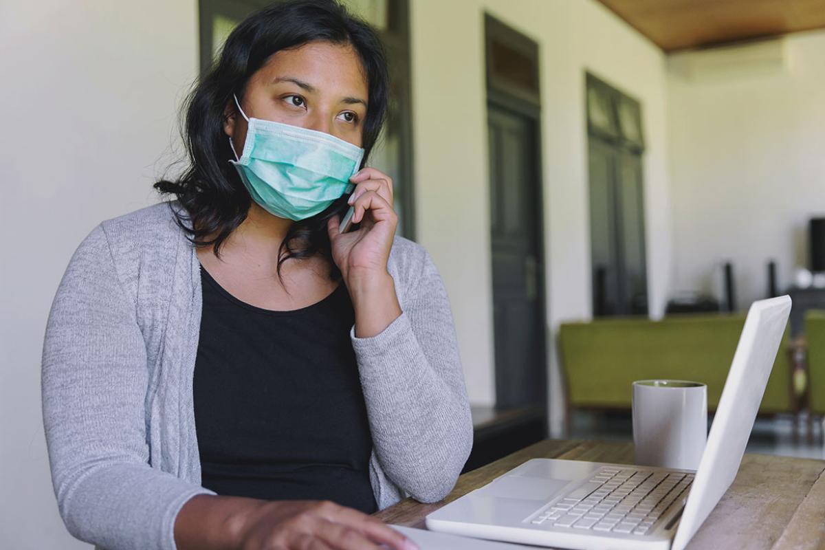 Masked person on the phone and sitting in front of a laptop