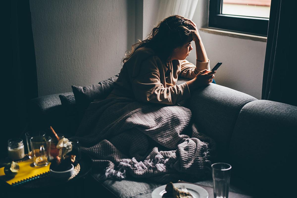 Person sitting in a dark room, head in hand, looking out a window