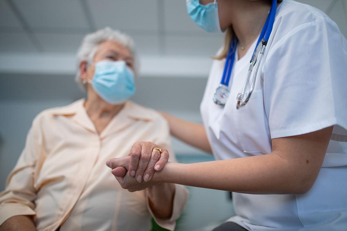 Health care worker holding hands with elderly patient in examination room