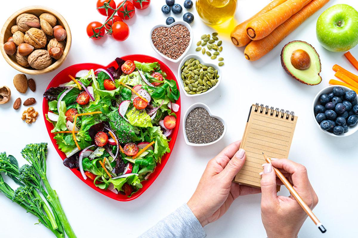 Heart shape plate with healthy salad surrounded by fruit and vegetables