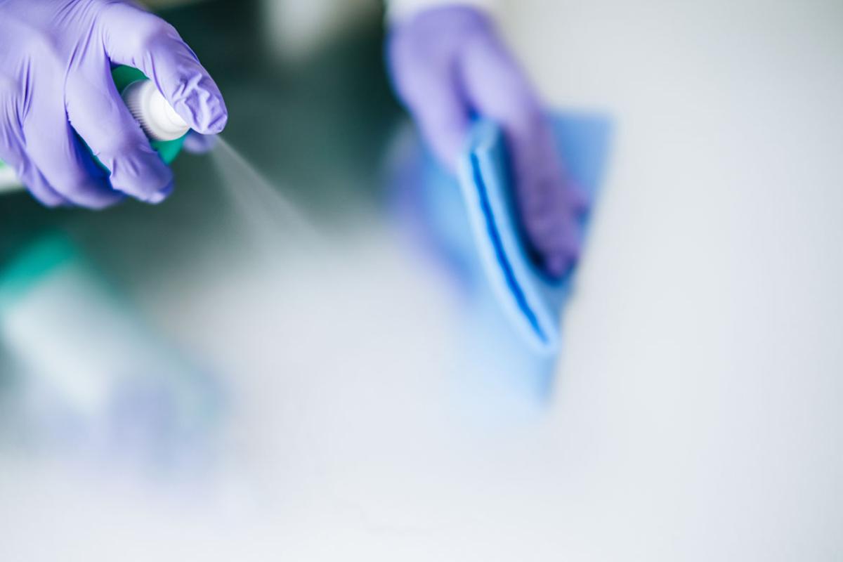 Gloved person spraying and wiping cleaning solution