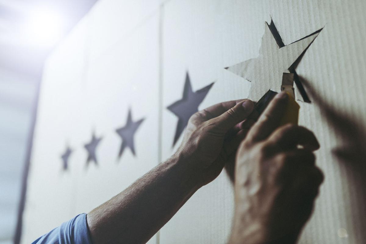 Hands using a yellow cutter to cut five stars from a cardboard box