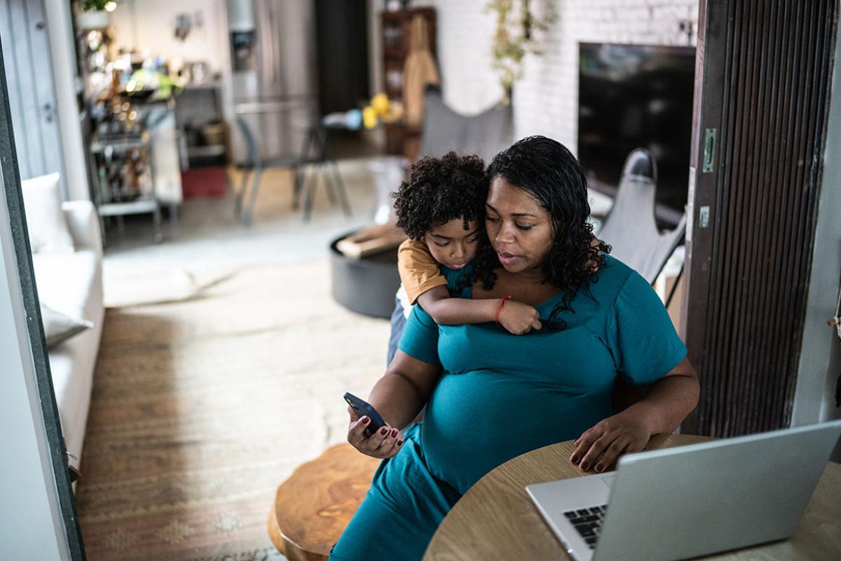 Pregnant person using laptop at home with child