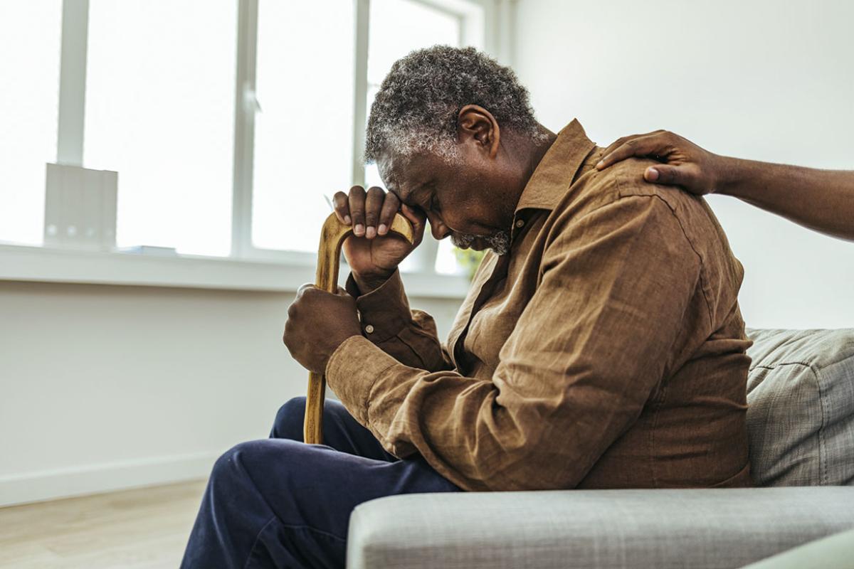 Seated elderly person with head on cane