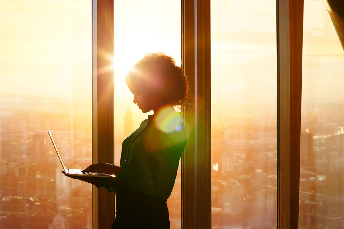 Person holding a laptop at window in morning sun