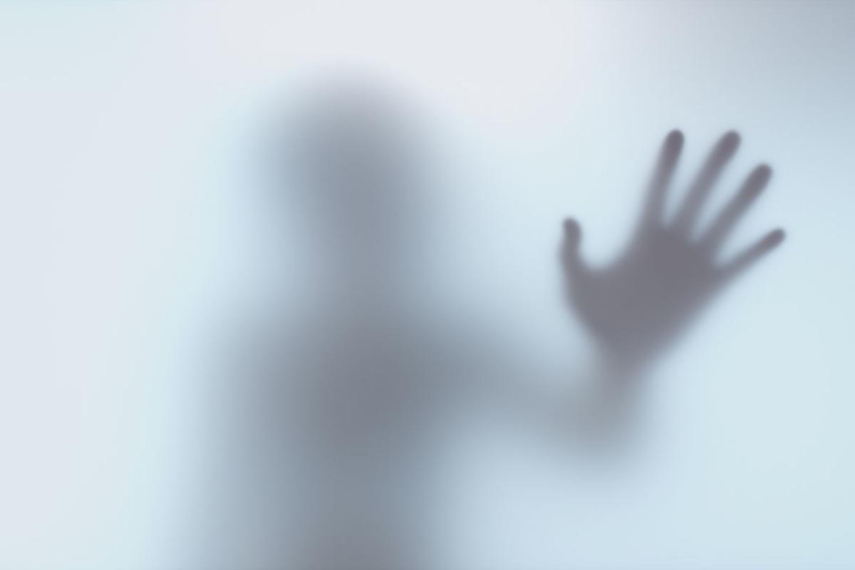 Shadow hand of figure behind frosted glass