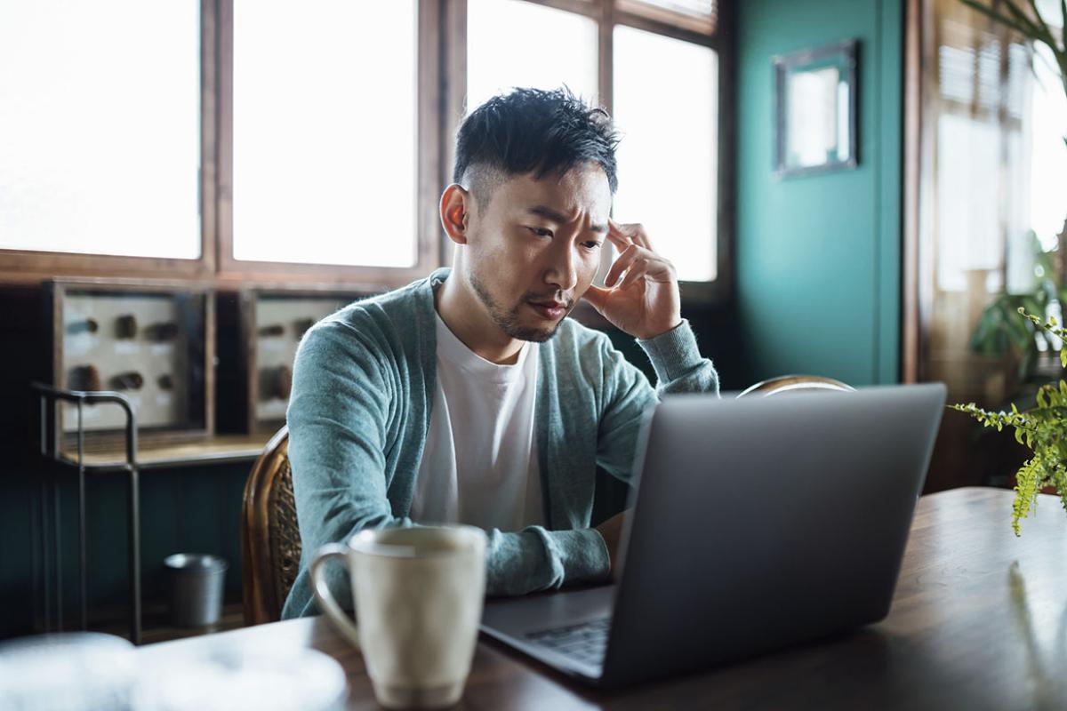 Young man with hand on head, using laptop computer