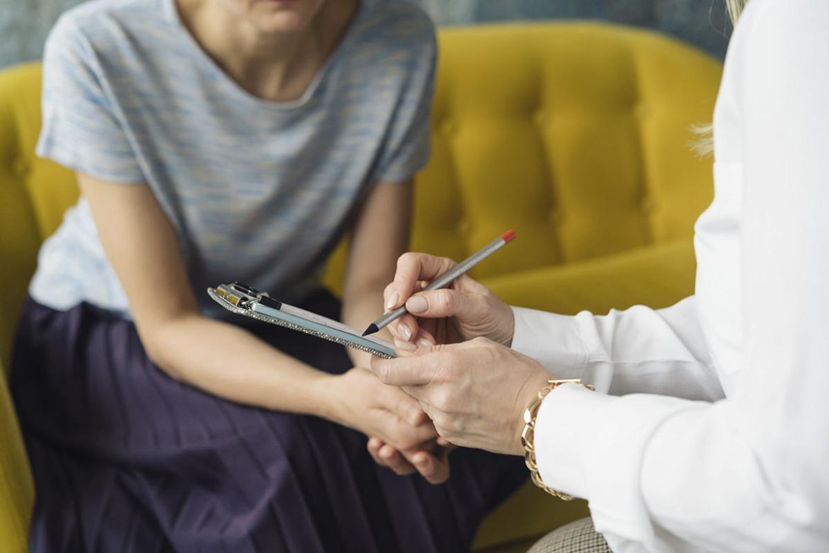 Person in conversation with a patient writes on a clip board