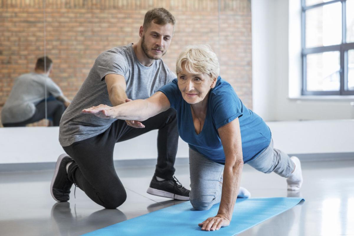 Senior woman being helped by her trainer in doing yoga workout at gym