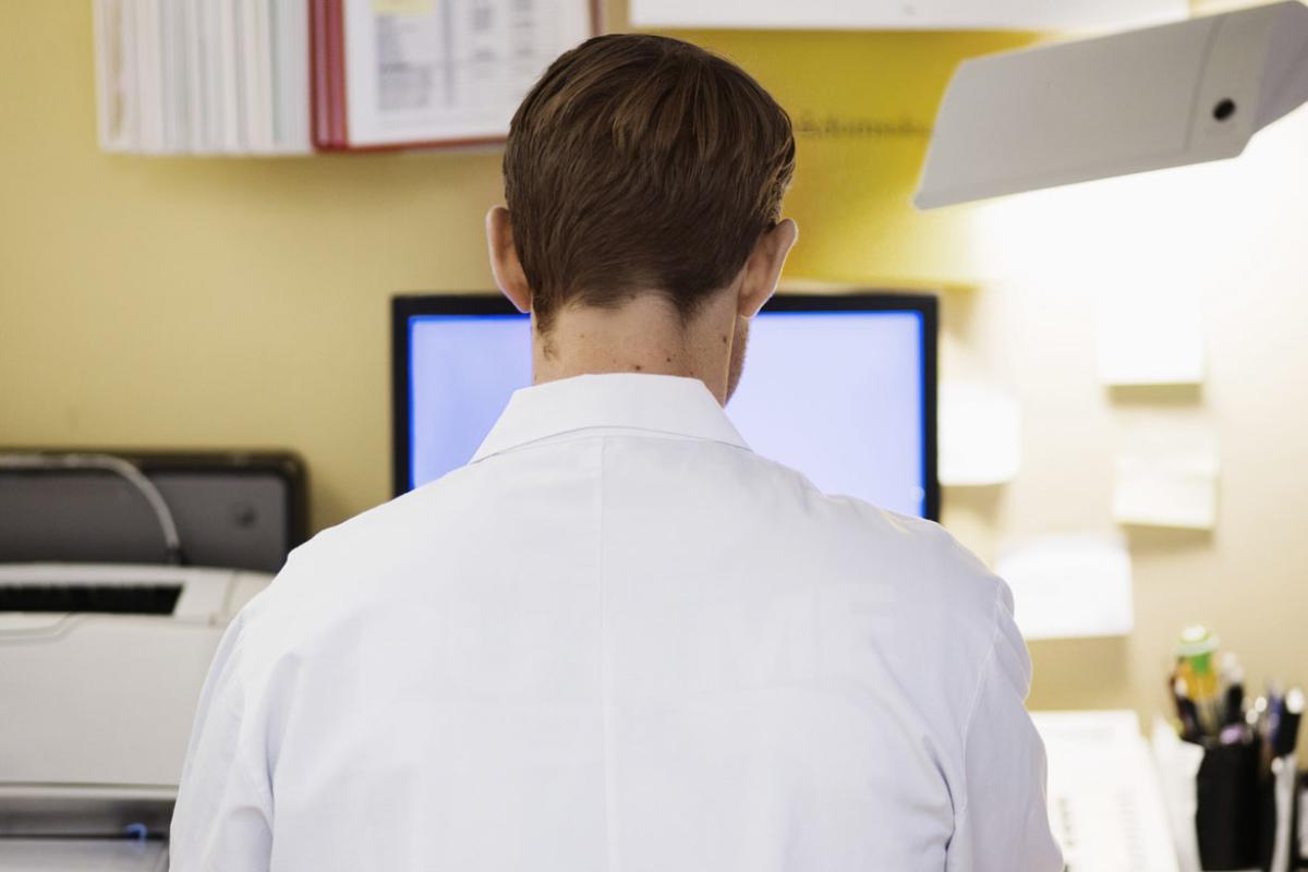 Rear view of mid adult male doctor using computer in clinic