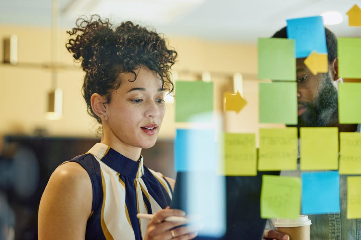 A man and a woman are standing in front of a glass wall writing on sticky notes