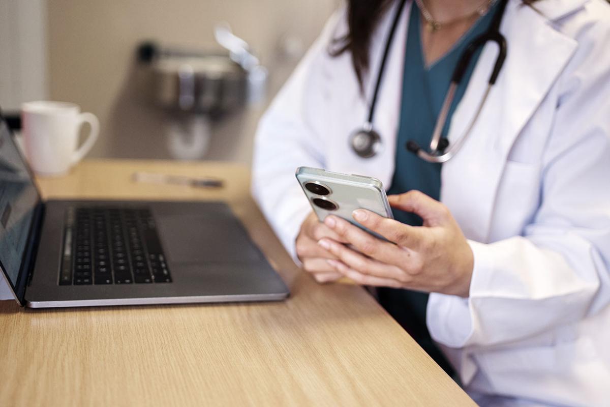 Doctor using a phone and laptop at a desk in a hospital