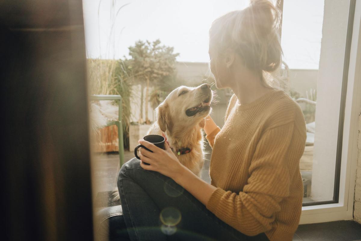 Young woman holding a mug and petting a dog