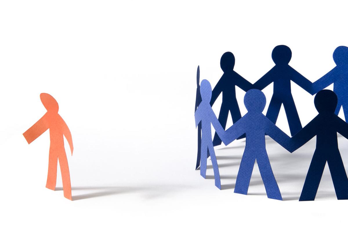 Paper person with dejected stance off to the side of a circle of paper people