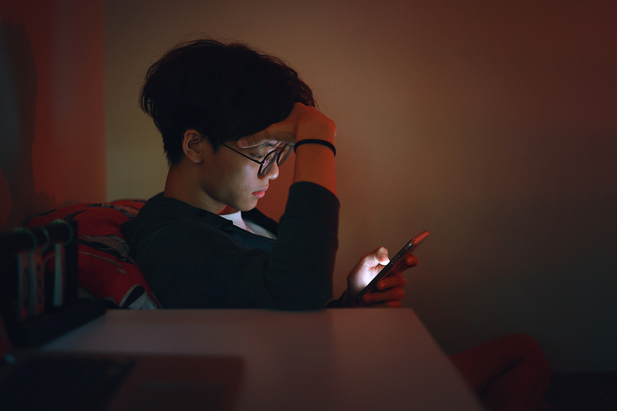 Young person scrolls through phone in a dimly lit room