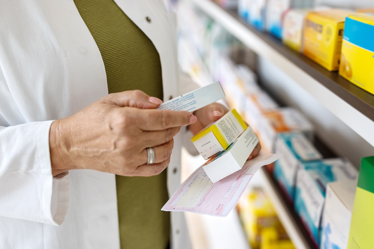 Pharmacist holding prescriptions in front of a storage shelf