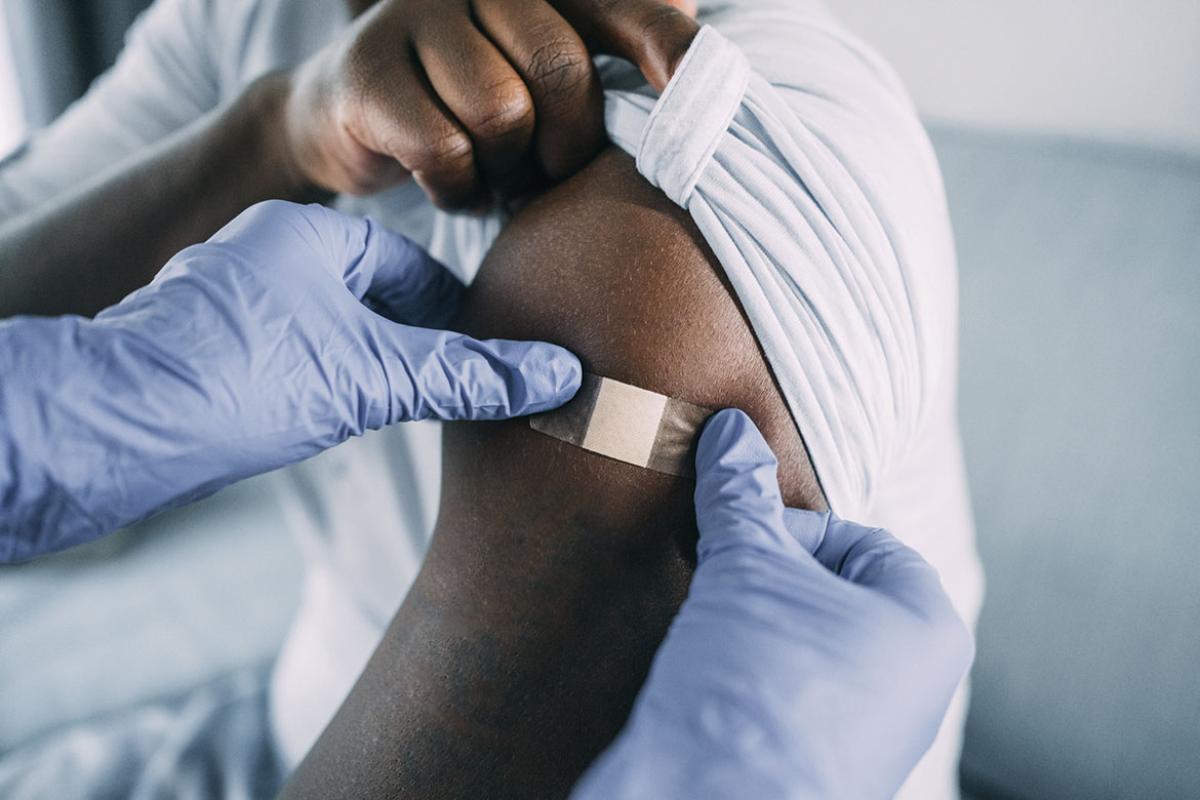 Health care worker applies adhesive bandage to patient's arm
