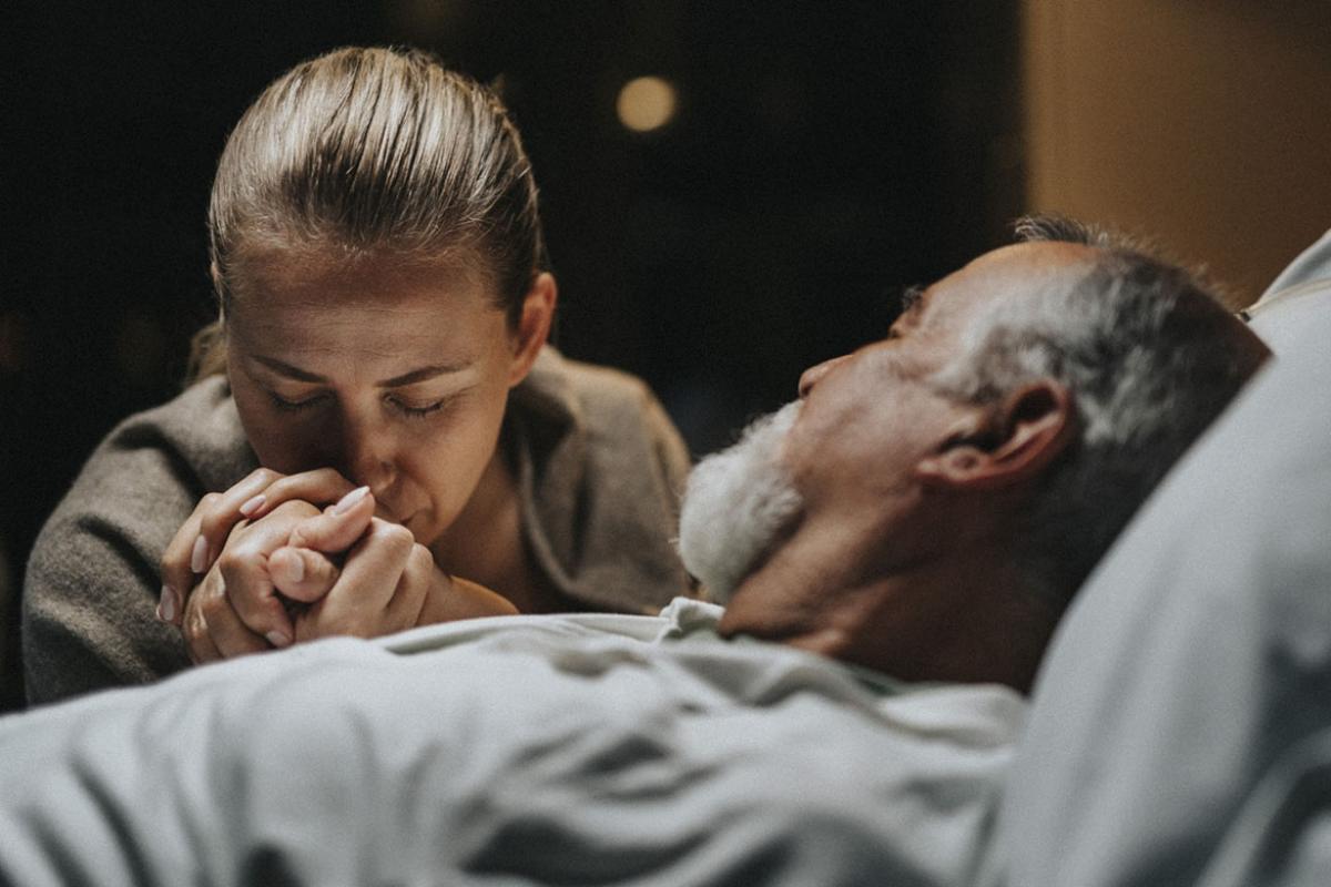 Woman gives a comforting hand hold to a man lying in a hospital bed