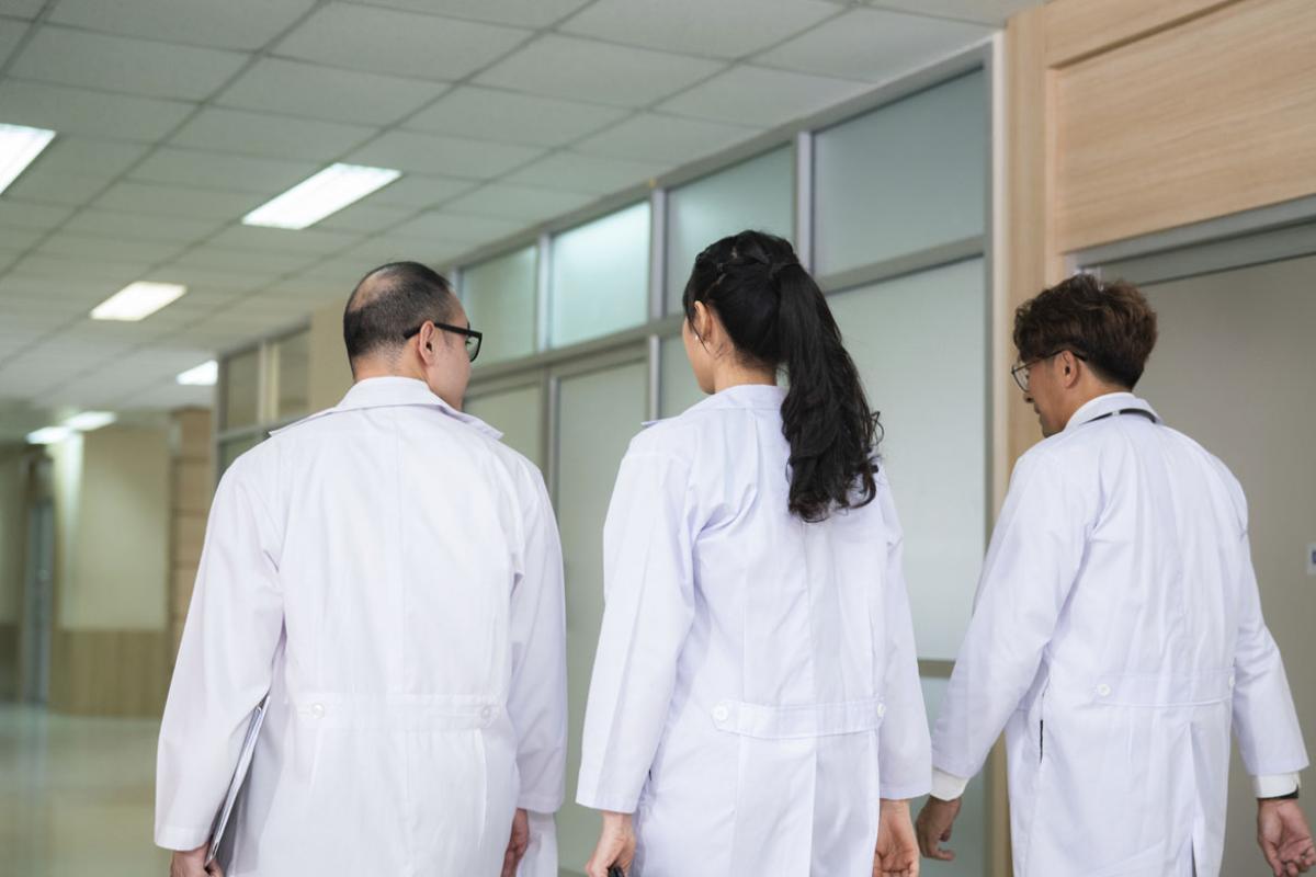 Three doctors in discussion walk down a hallway