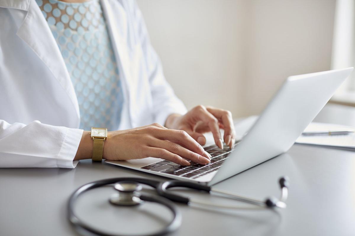 Doctor typing on laptop by stethoscope at desk