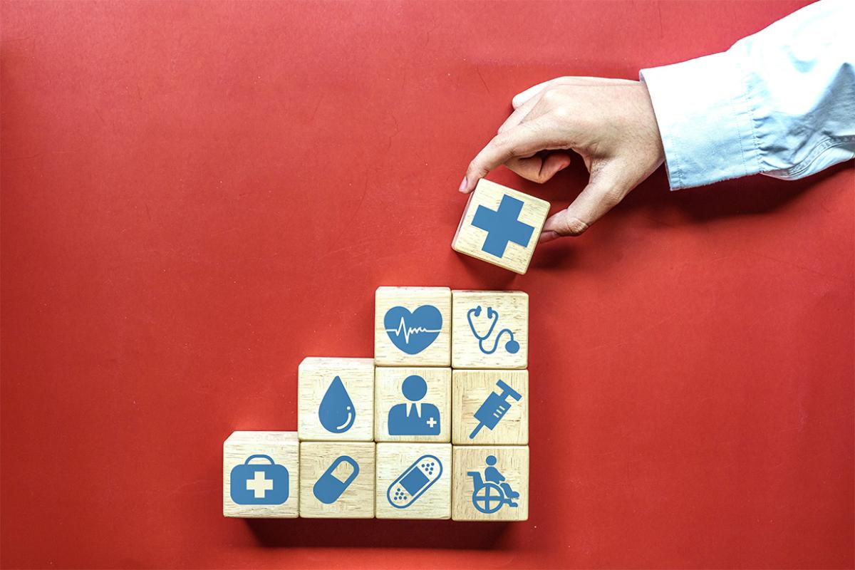 Hand stacking a series of blocks with health care icons