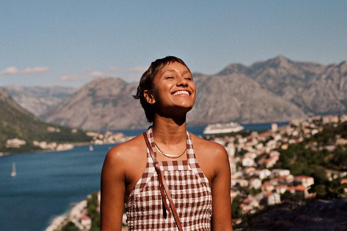 Smiling woman enjoying sunlight against mountain range and sea