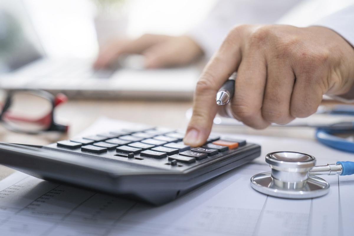 Hand using calculator with stethoscope nearby