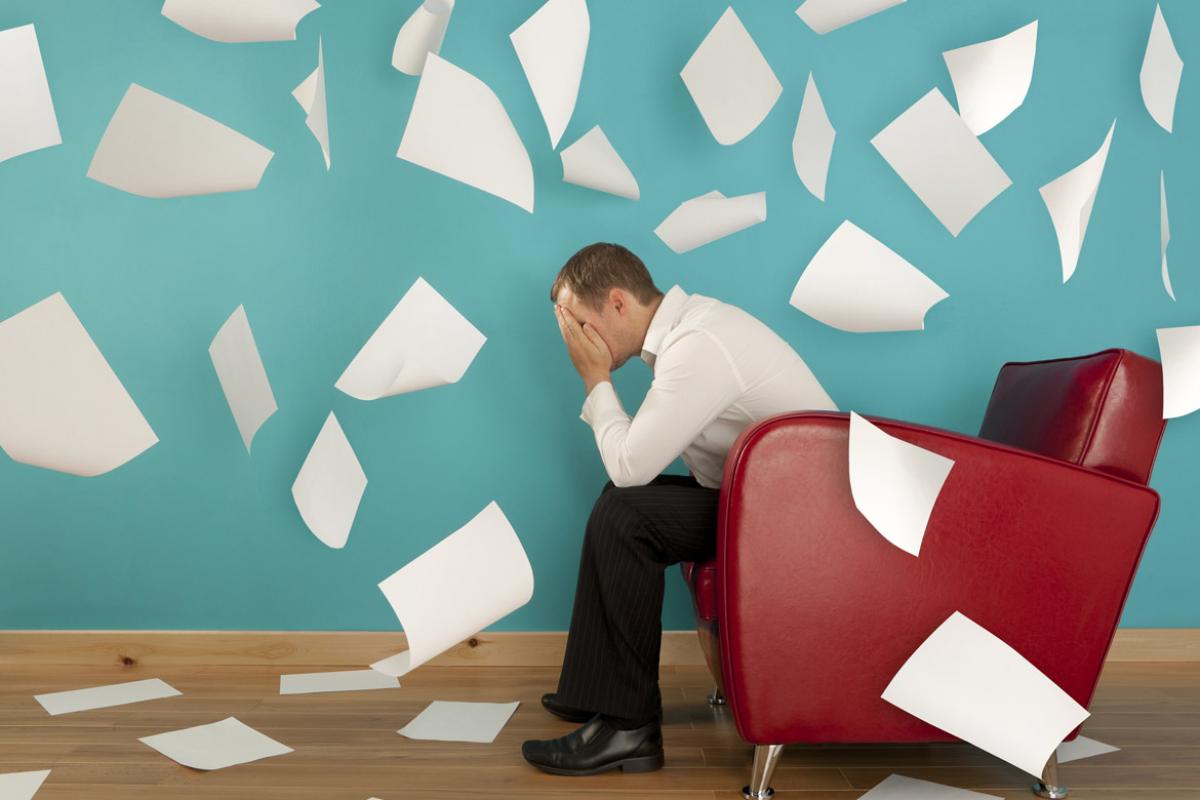 Worried man sitting in an armchair with paper flying around