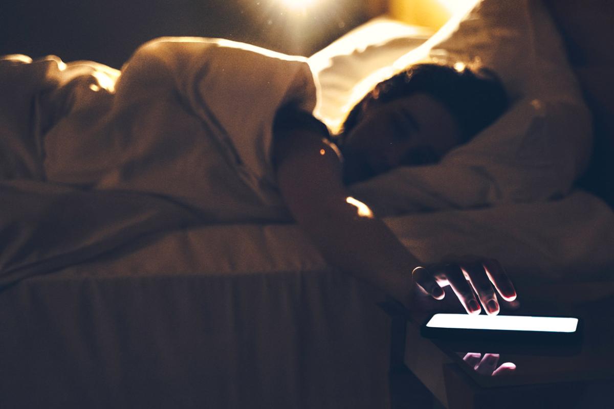 Person in bed reaches for illuminated smartphone