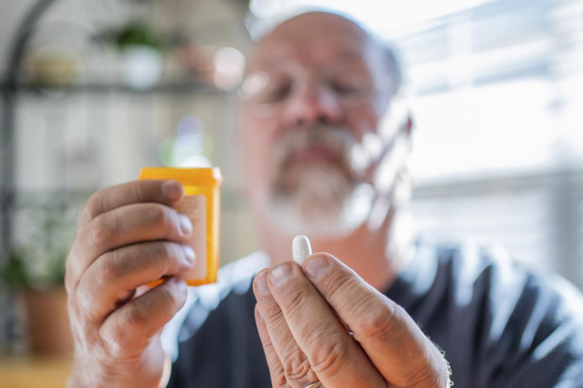 Patient holds a pill in one hand and a prescription bottle in another