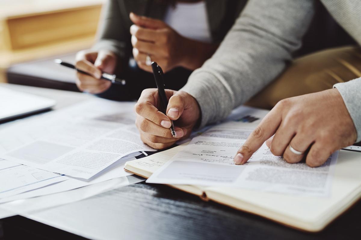 One hand points to a form while the other holds a pen