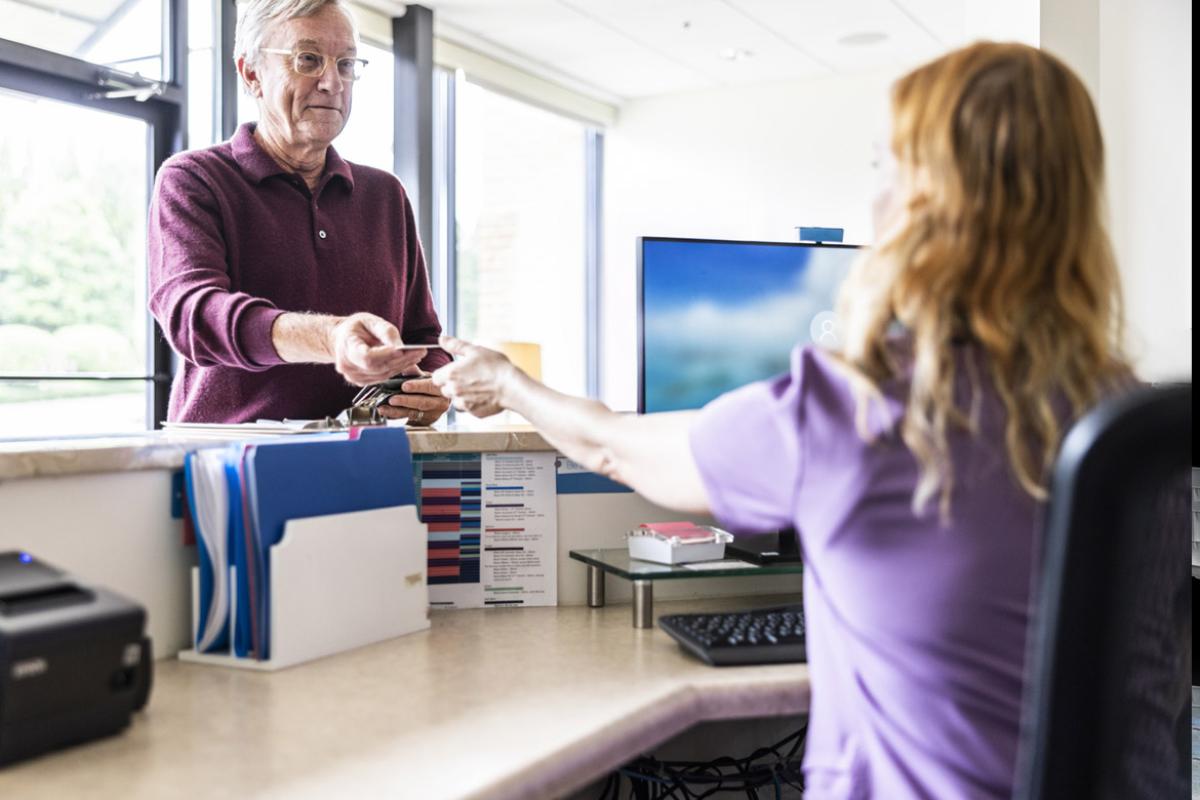 Patient hands card to front-desk employee at a doctor's office